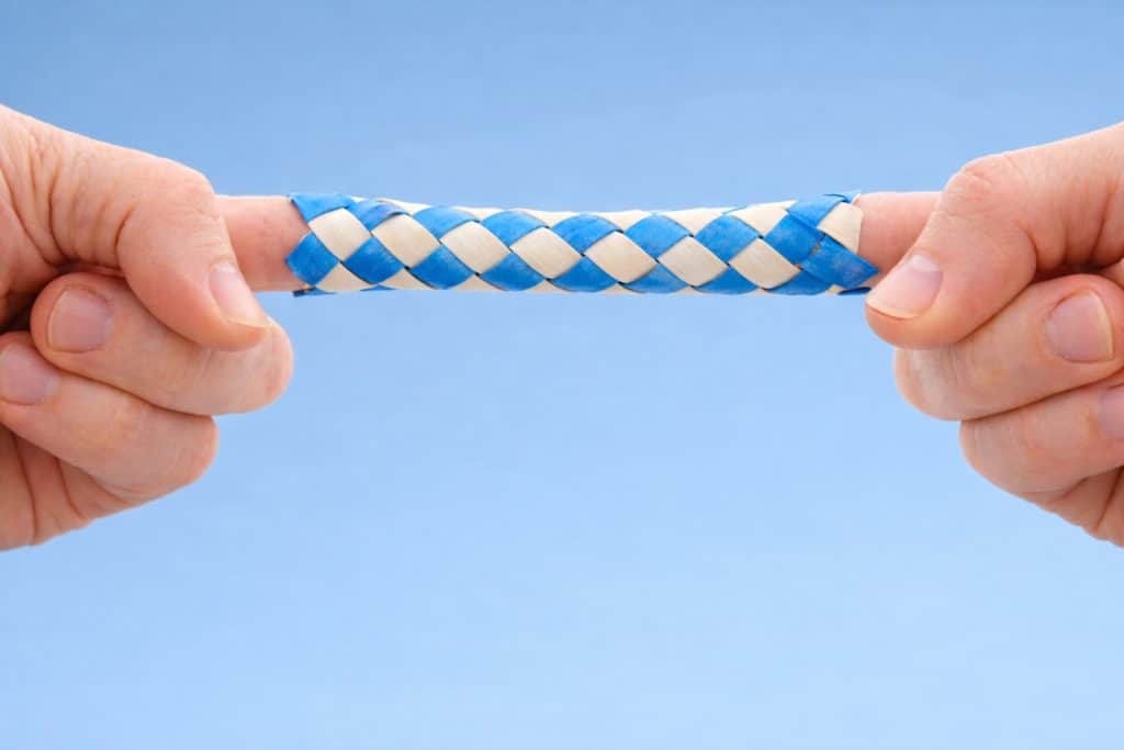 Close-up of two hands pulling against a blue Chinese finger trap with index fingers inserted, showing how it tightens when pulled apart.